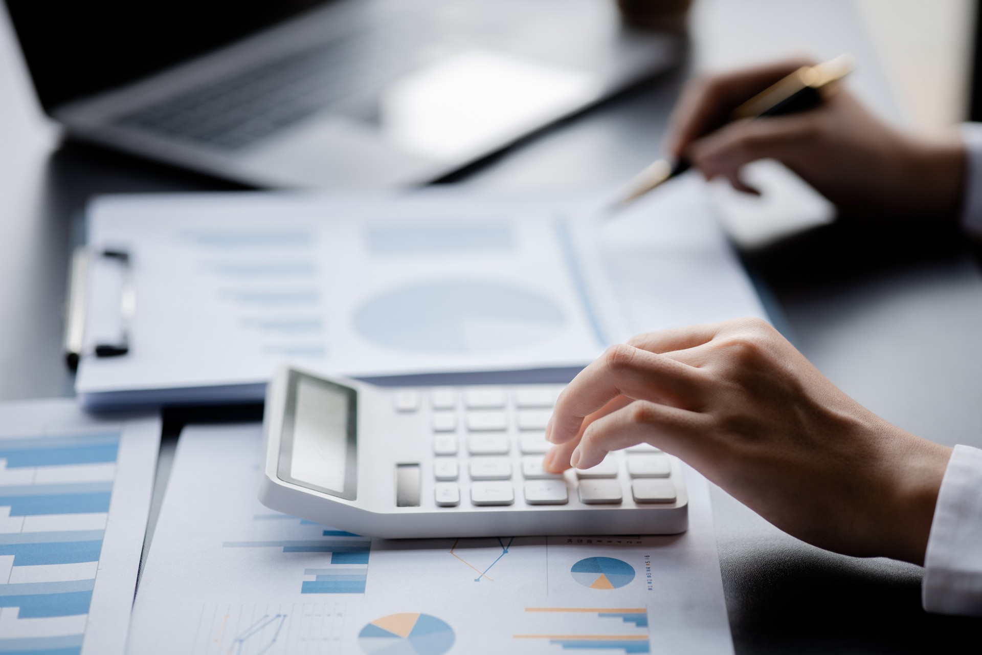 Businessman is using a calculator to calculate company financial figures from earnings papers, a businessman sitting in his office where the company financial chart is placed.